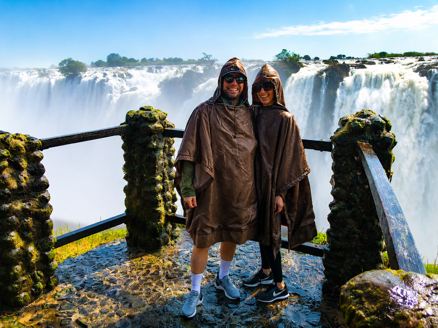 Couple taking photos during a private guided Victoria Falls tour with the spectacular waterfall and rainforest scenery in the background.