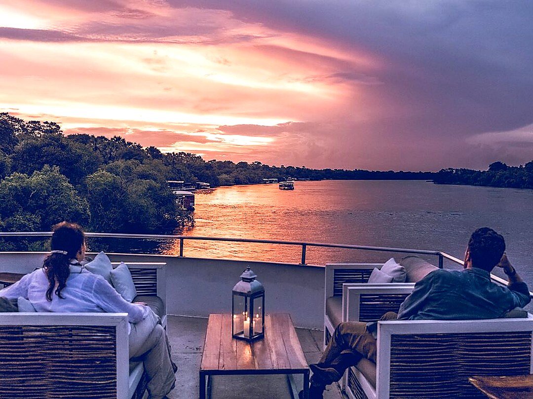 A couple enjoying a Zambezi River sunset cruise near Victoria Falls with beautiful views of the river and golden evening sky