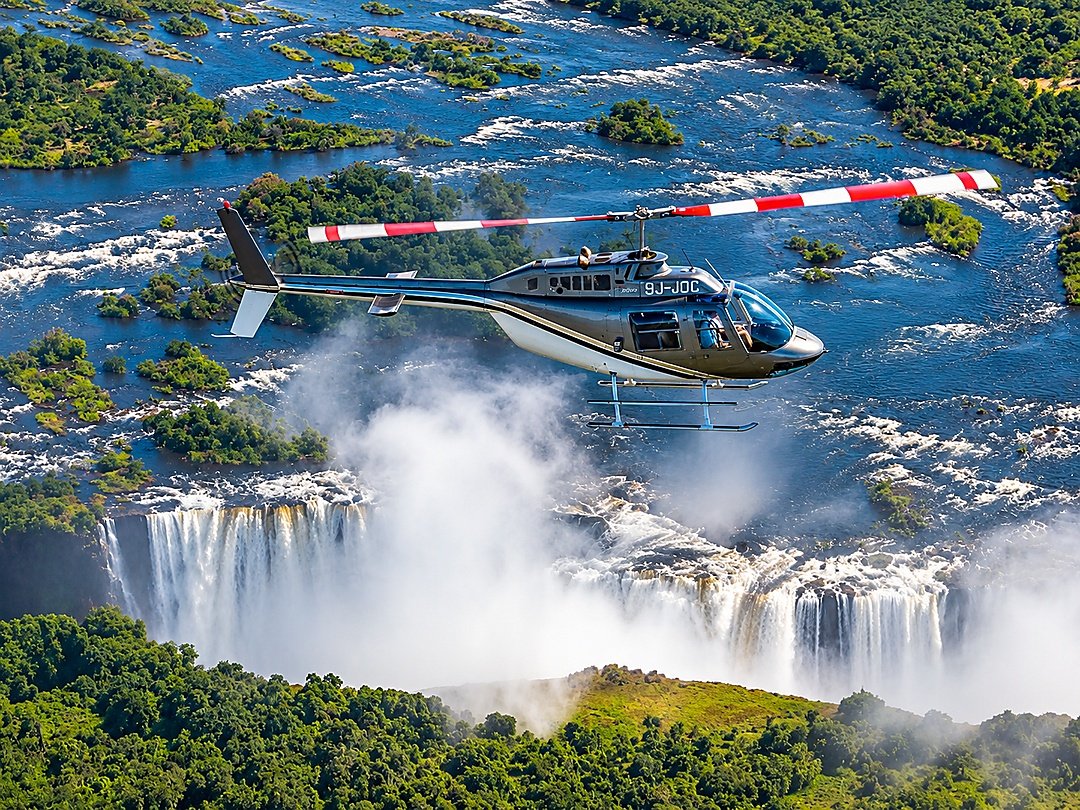 Tourists enjoying a spectacular Flight of Angels over Victoria Falls, admiring breathtaking aerial views of the waterfall, Zambezi River, gorge, and surrounding landscape.