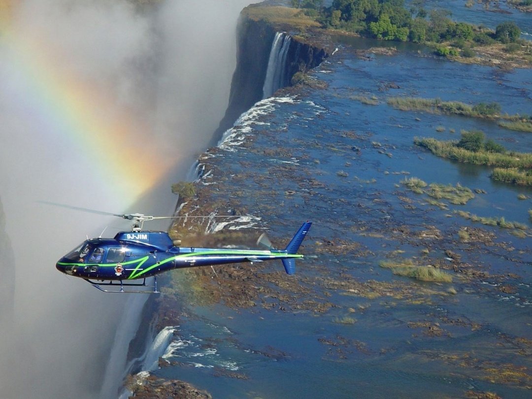A helicopter flying over Victoria Falls, offering spectacular aerial views of the cascading waterfall, Zambezi River, surrounding gorge, and lush landscape.