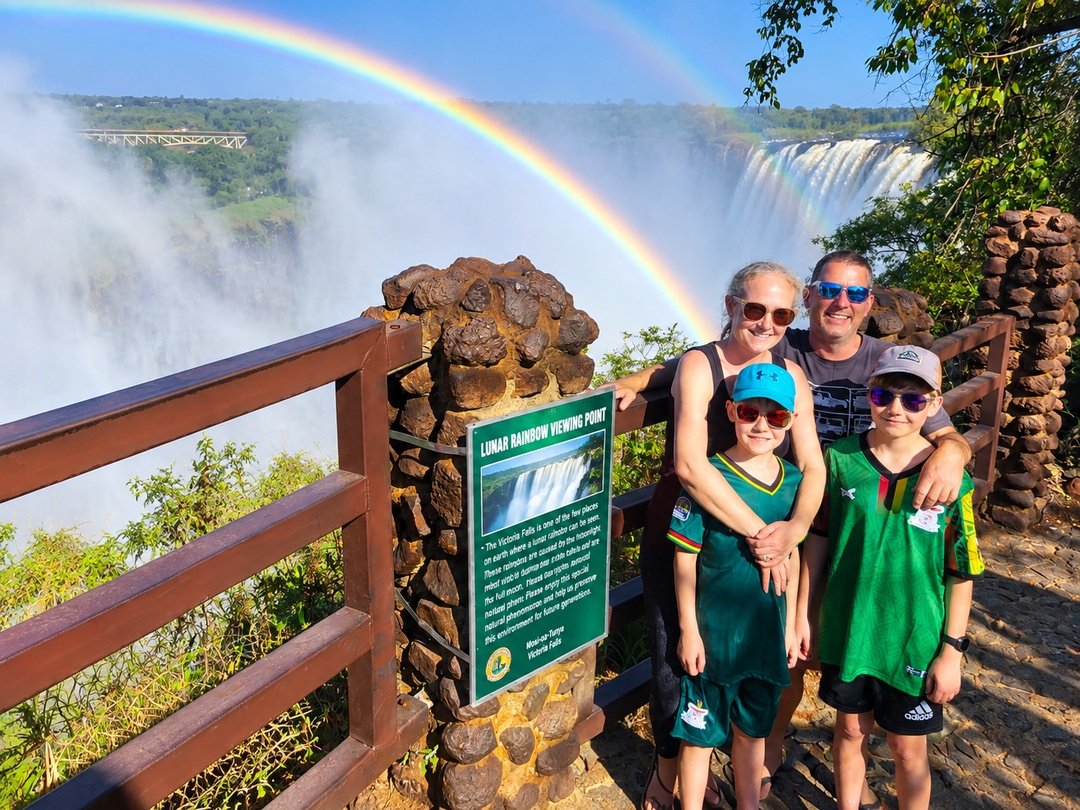 A family enjoying a private safari to Victoria Falls, admiring the spectacular waterfall, Zambezi River scenery, mist, lush surroundings, and breathtaking views.