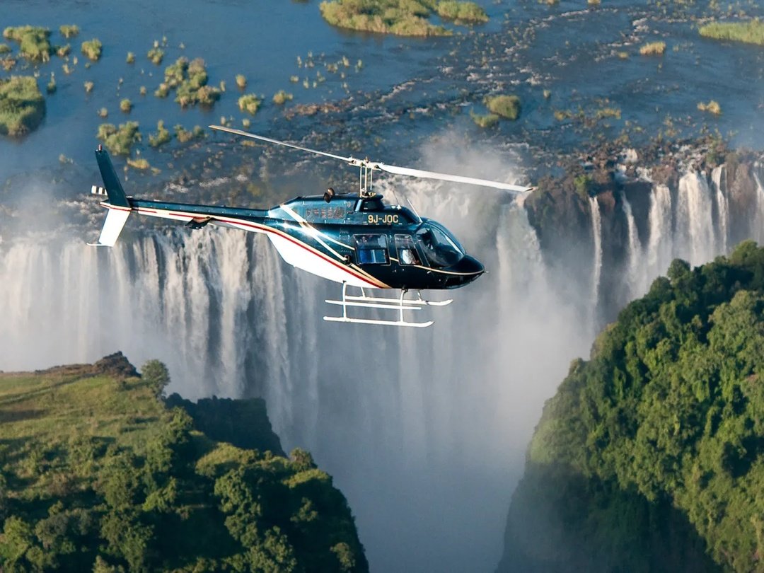 Tourists enjoying a helicopter ride over Victoria Falls, capturing breathtaking aerial photographs of the spectacular waterfall, Zambezi River and surrounding landscapes from above.