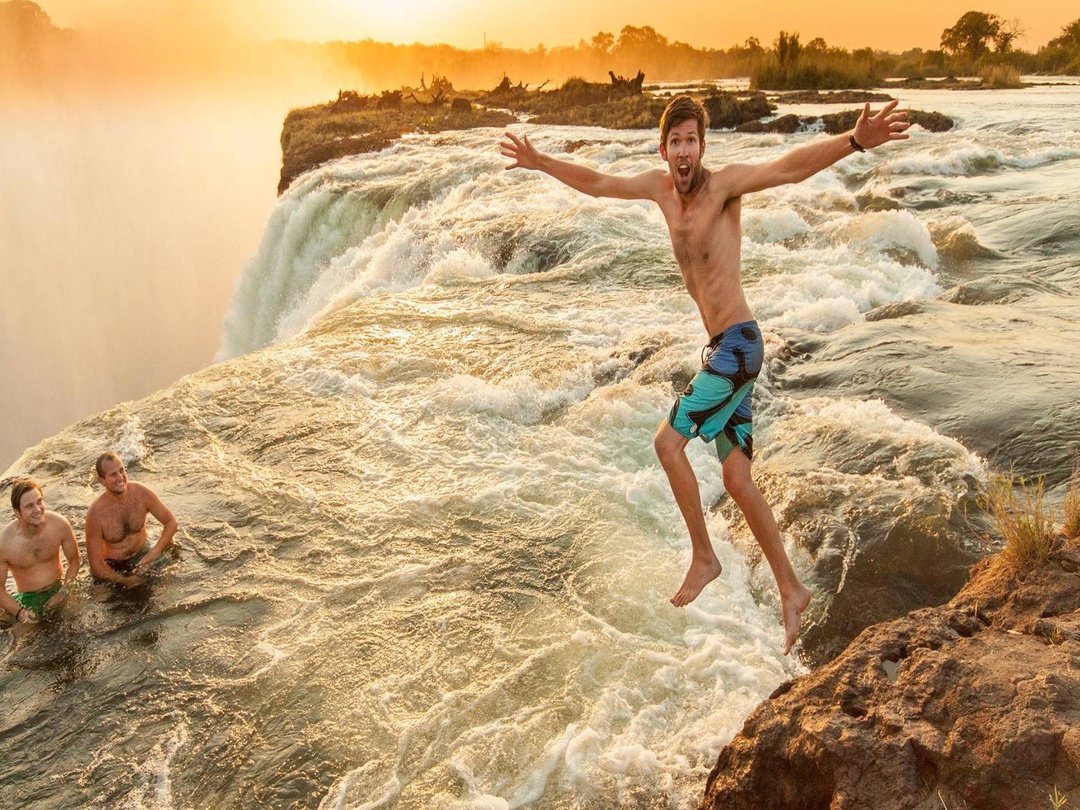 Tourists enjoying Victoria Falls from Livingstone Island, taking in the spectacular Zambezi River views and powerful waterfall surrounded by natural scenery.