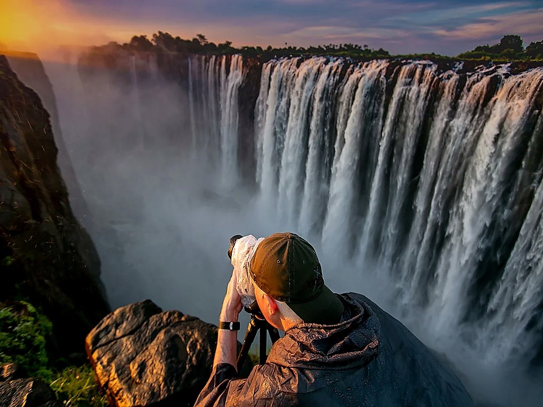 A photographer taking photos of Victoria Falls, capturing the spectacular waterfall, mist, dramatic landscape, and powerful Zambezi River scenery.
