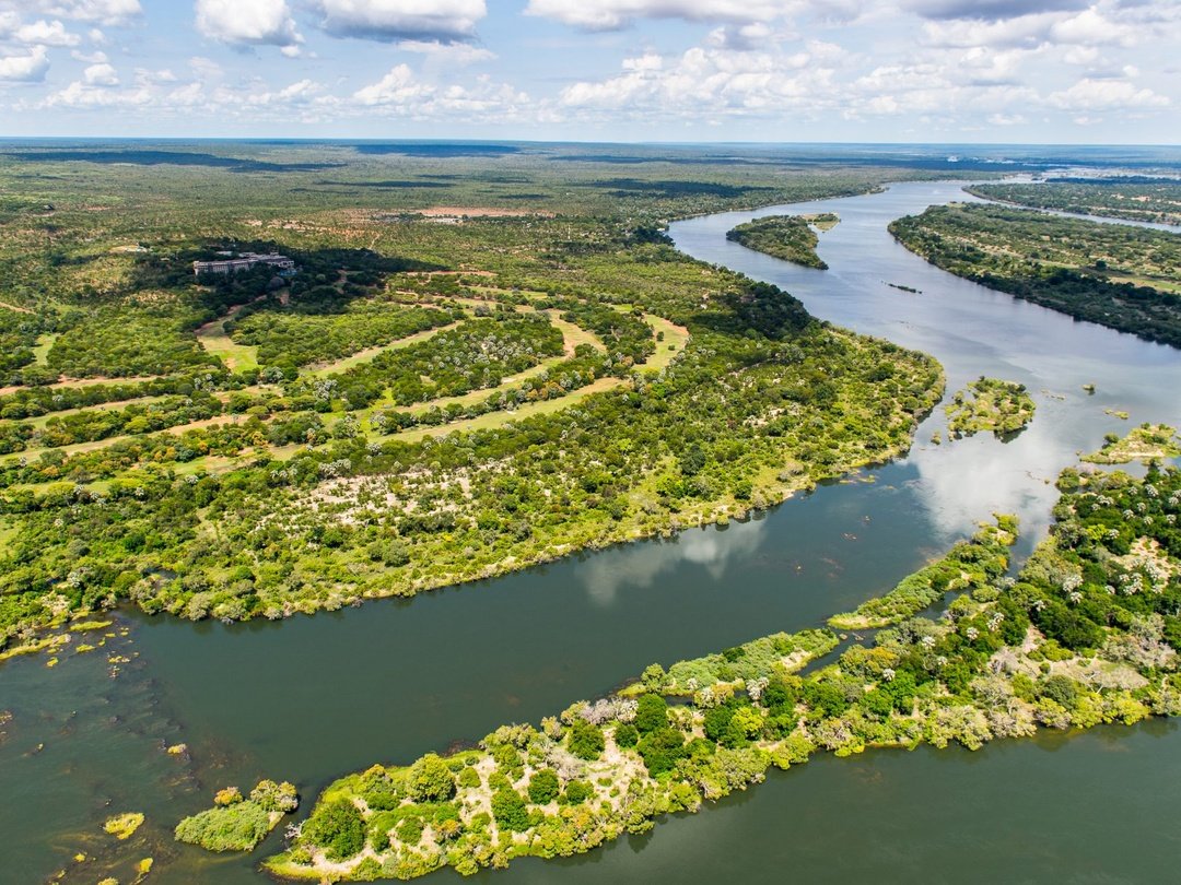 Aerial view of the Zambezi River winding through lush green islands and vegetation near Victoria Falls, showcasing the river’s expansive channels and surrounding African landscape.