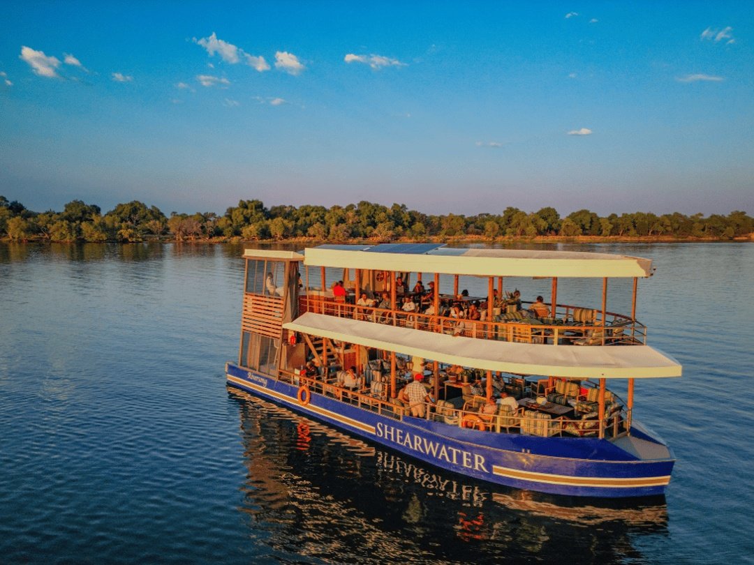Tourists enjoying a Zambezi River sunset cruise, relaxing aboard a boat while watching the golden sunset over the peaceful river and surrounding African wilderness.
