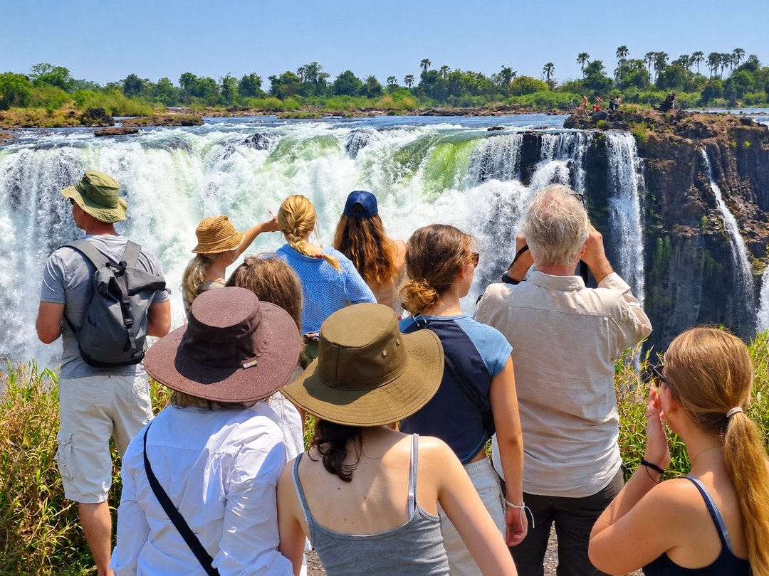 Tourists visiting Victoria Falls admire the spectacular Zambezi River waterfall, enjoying breathtaking views, powerful cascading water, lush surroundings, and an unforgettable sightseeing experience together.