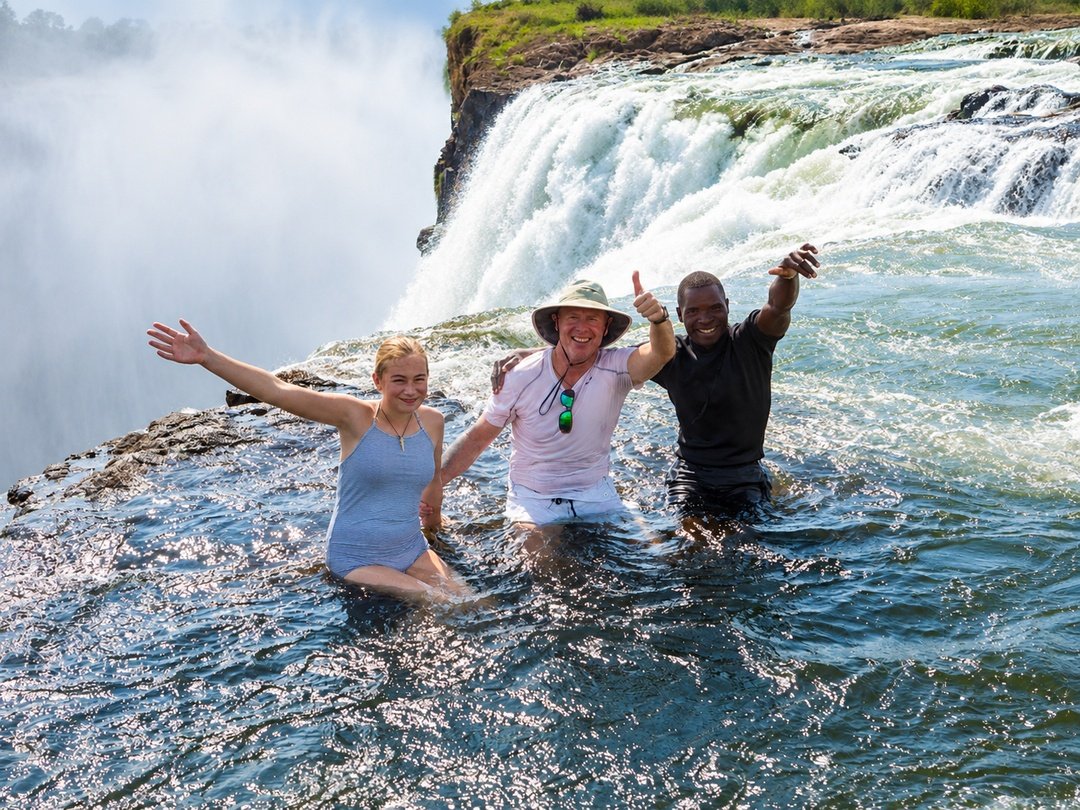 Tourists swimming at Victoria Falls during a luxury safari, enjoying the refreshing Zambezi River waters and spectacular waterfall scenery in Zimbabwe.