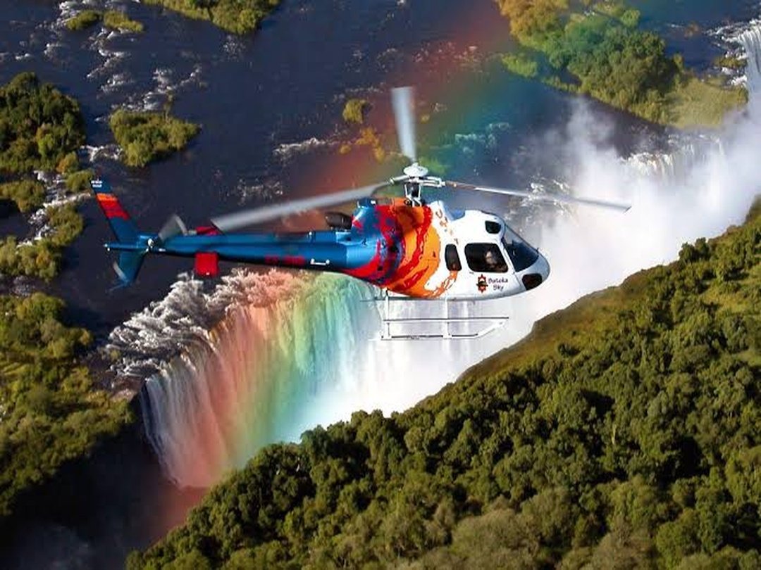 Tourists enjoying a scenic helicopter tour over Victoria Falls, flying above the spectacular waterfall, Zambezi River and surrounding landscapes while experiencing breathtaking aerial views of this African natural wonder.