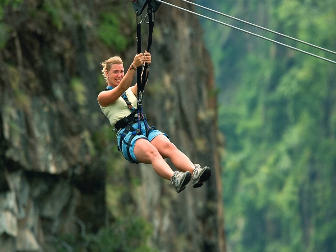 A tourist enjoying an exhilarating ziplining adventure over the Batoka Gorge near Victoria Falls, taking in spectacular views of the dramatic gorge, surrounding forest and Zambezi River landscape.
